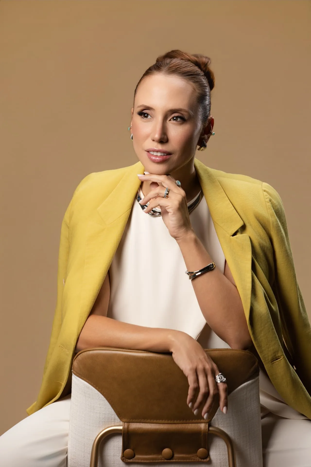 Milena Costa sentada, blazer amarelo sobre look off-white